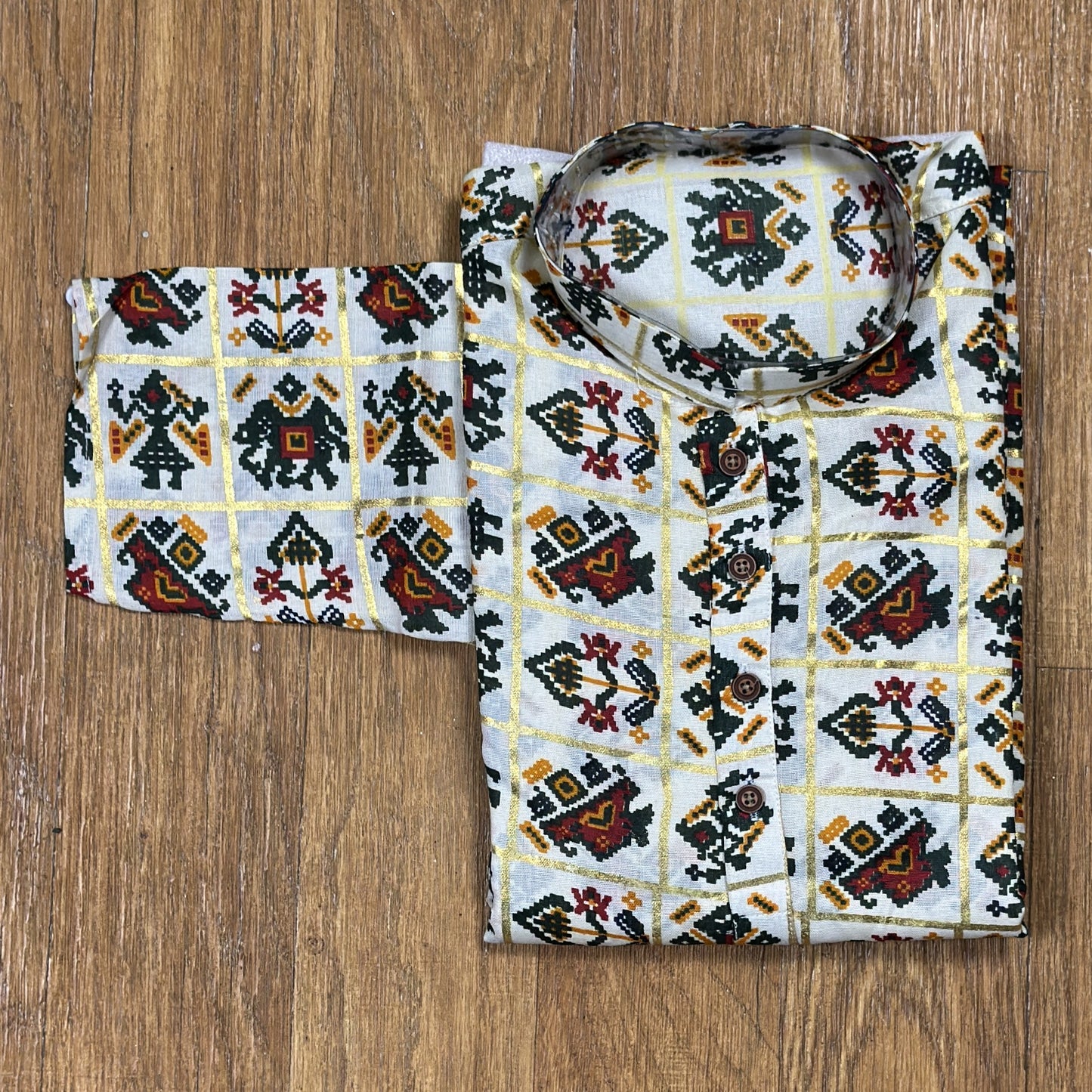 Folded mandarin collar shirt with green, red, and yellow geometric floral print on white fabric, placed on wooden floor