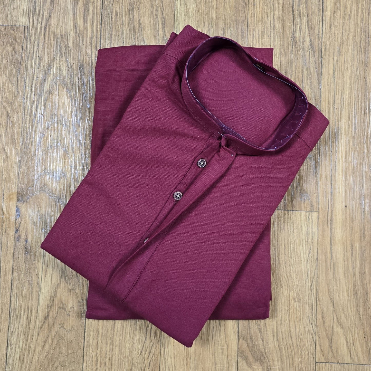 Folded maroon mandarin collar shirt on wooden floor