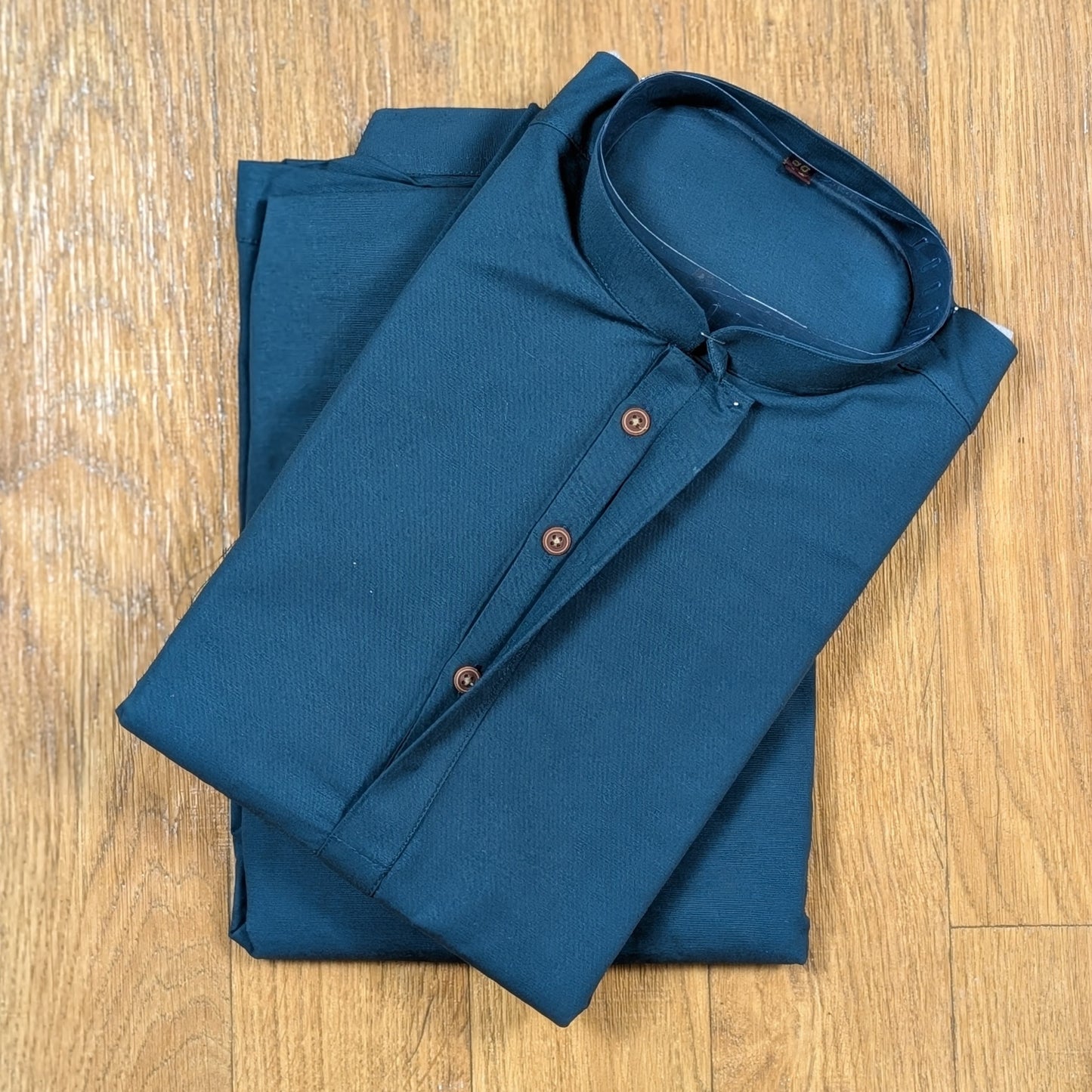 Folded Ocean Blue mandarin collar kurtawith brown buttons on wooden floor