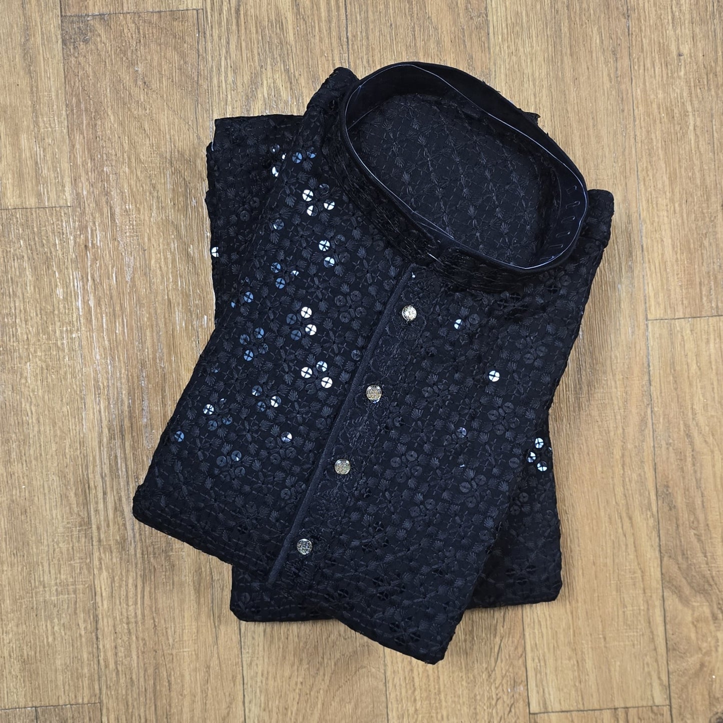 Folded black sequined garment on a wooden floor