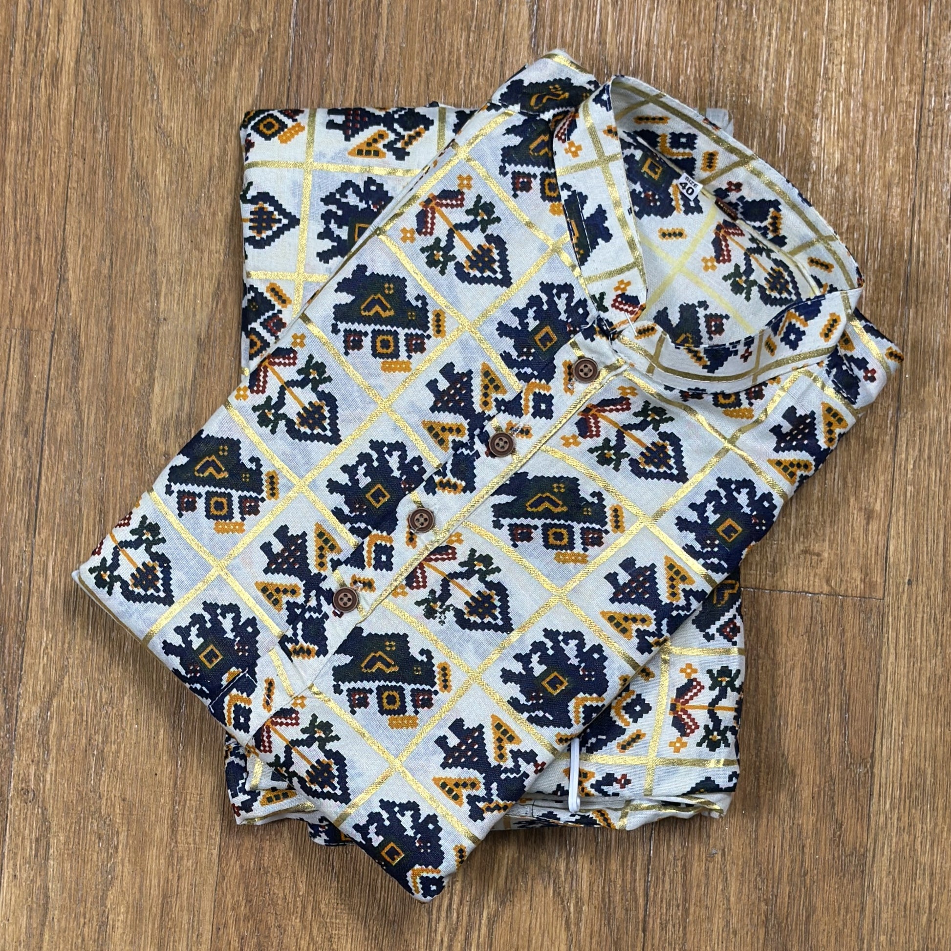 Folded mandarin collar shirt with navy blue, yellow, and maroon geometric floral print on white fabric, placed on wooden floor