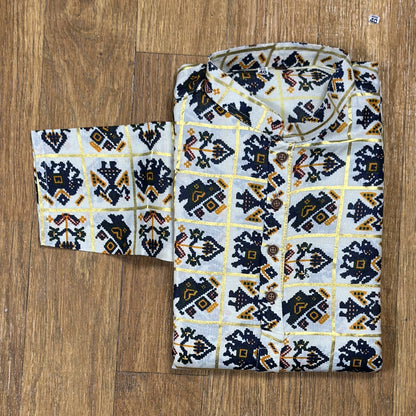 Folded mandarin collar shirt with navy blue, yellow, and maroon geometric floral print on white fabric, placed on wooden floor