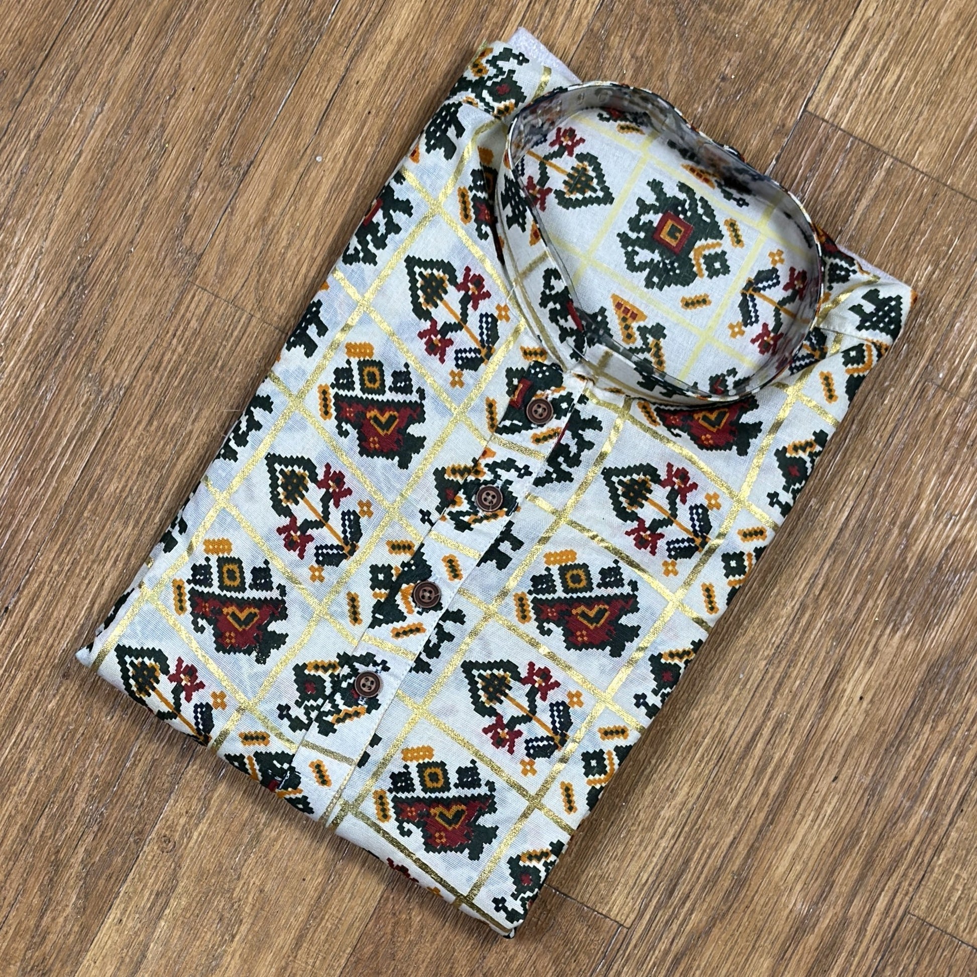 Folded mandarin collar shirt with green, red, and yellow geometric floral print on white fabric, placed on wooden floor
