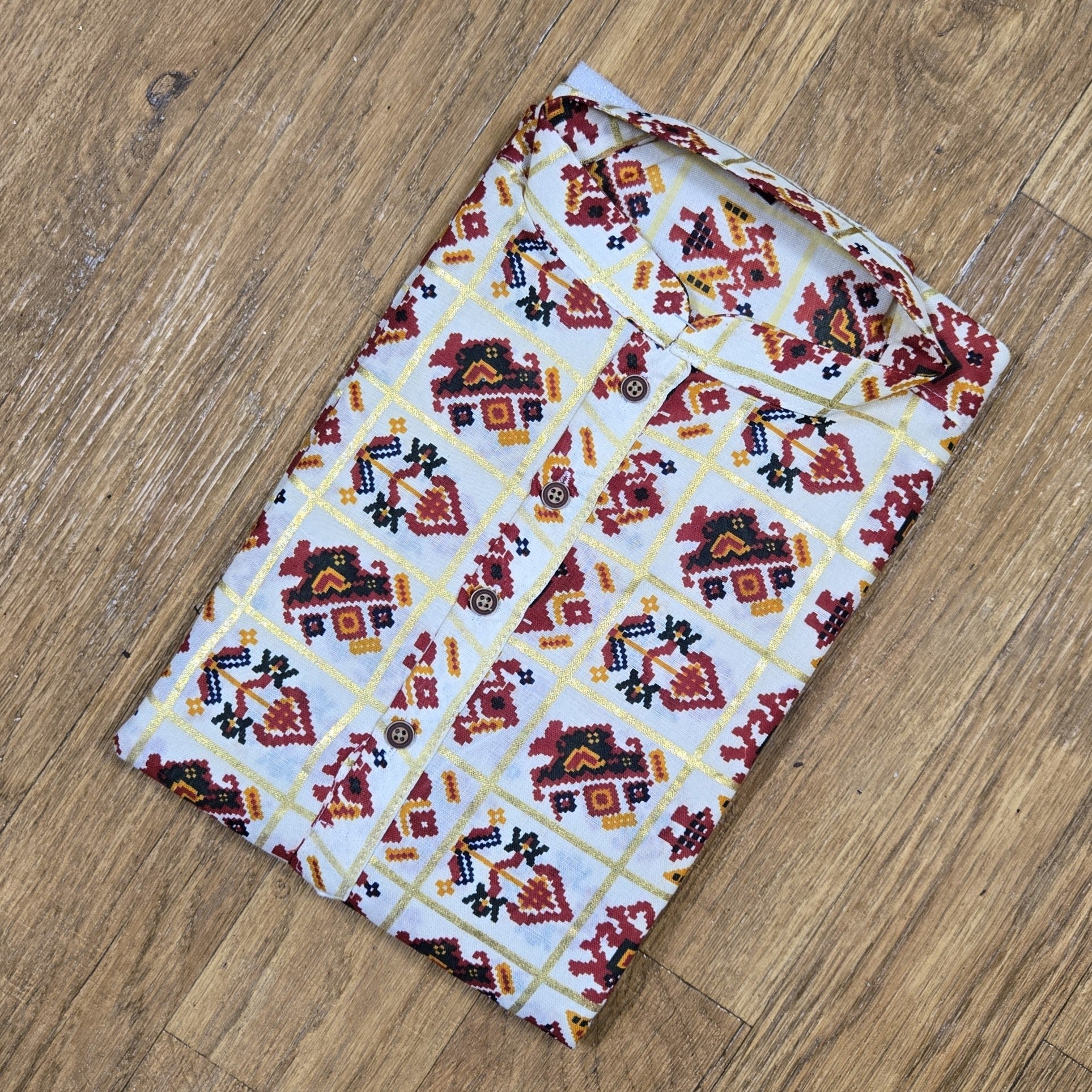 Folded mandarin collar shirt with red, yellow, and black geometric floral print on white fabric, placed on wooden floor