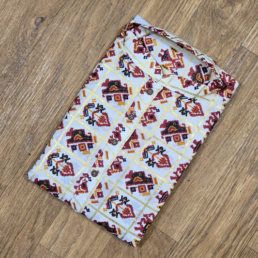 Folded mandarin collar shirt with red, yellow, and black geometric floral print on white fabric, placed on wooden floor