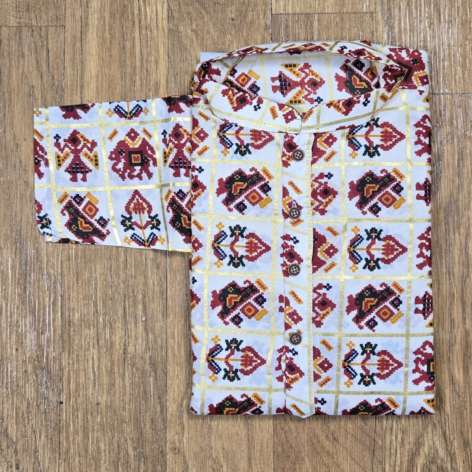 Folded mandarin collar shirt with red, yellow, and black geometric floral print on white fabric, placed on wooden floor