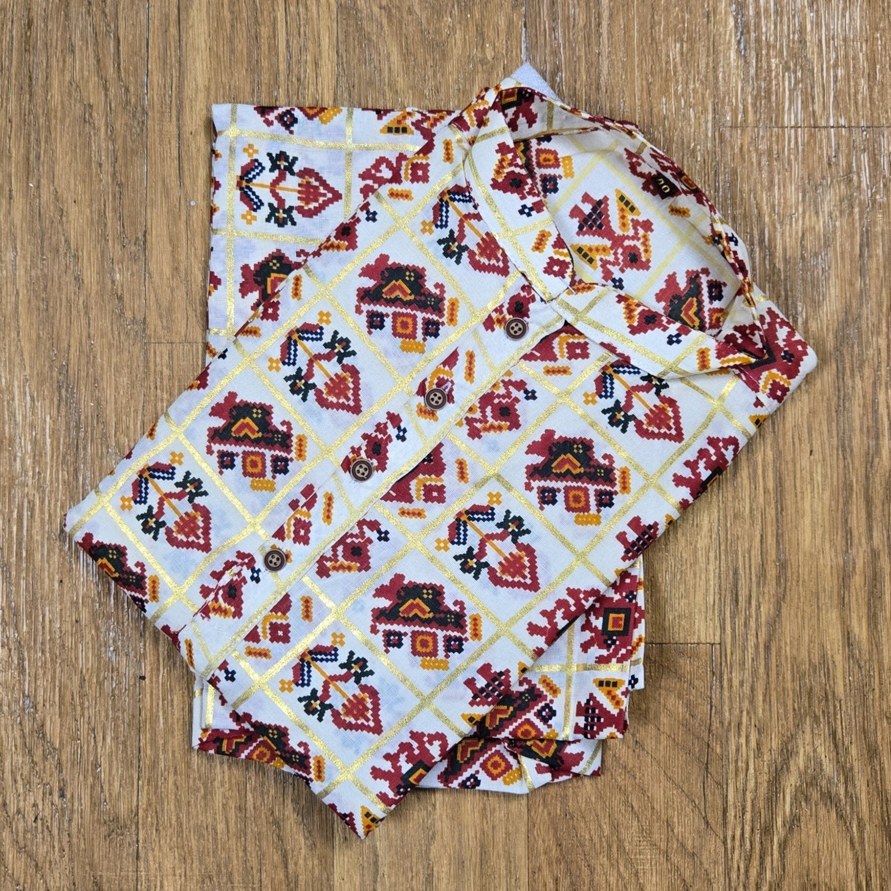 Folded mandarin collar shirt with red, yellow, and black geometric floral print on white fabric, placed on wooden floor