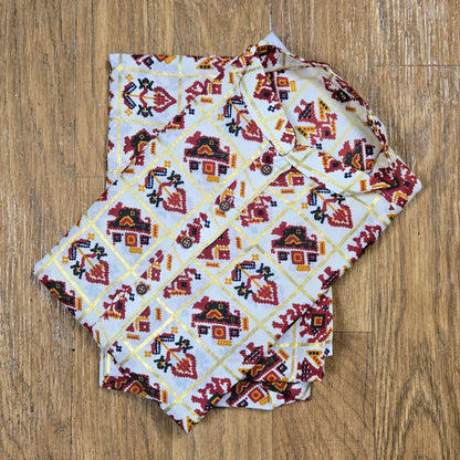 Folded mandarin collar shirt with red, yellow, and black geometric floral print on white fabric, placed on wooden floor