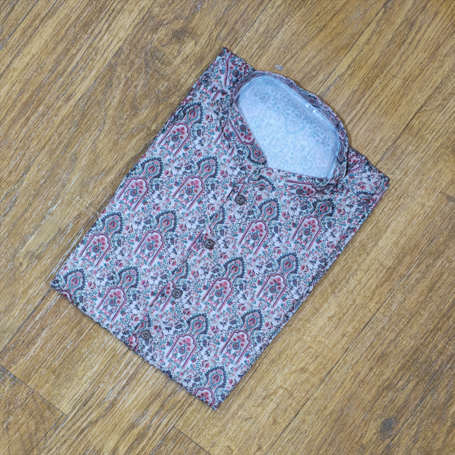 Folded mandarin collar shirt with intricate floral and paisley pattern in pink, green, and white on wooden floor