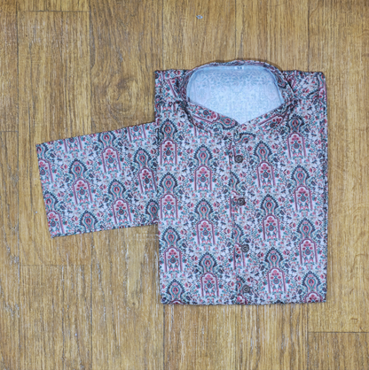 Folded mandarin collar shirt with intricate floral and paisley pattern in pink, green, and white on wooden floor