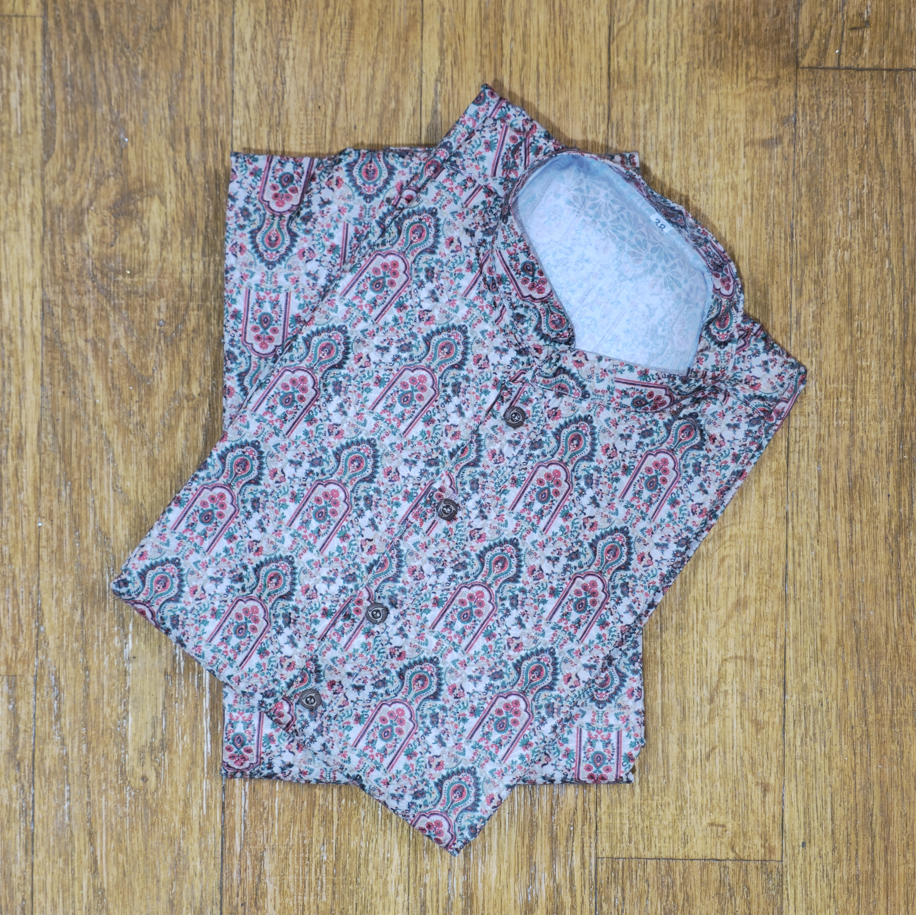 Folded mandarin collar shirt with intricate floral and paisley pattern in pink, green, and white on wooden floor