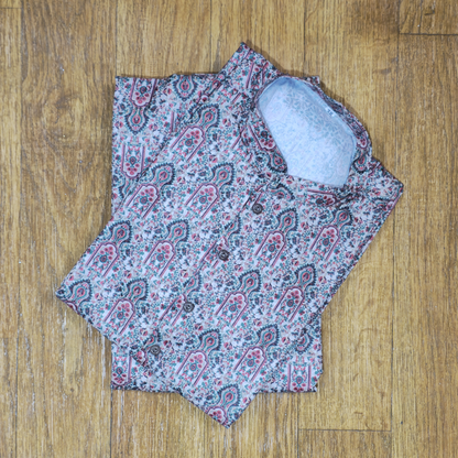 Folded mandarin collar shirt with intricate floral and paisley pattern in pink, green, and white on wooden floor