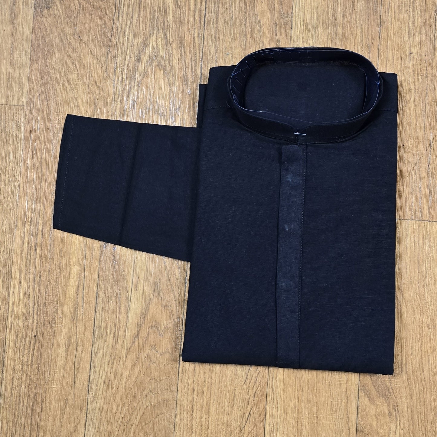 Folded black mandarin collar shirt with brown buttons on wooden floor
