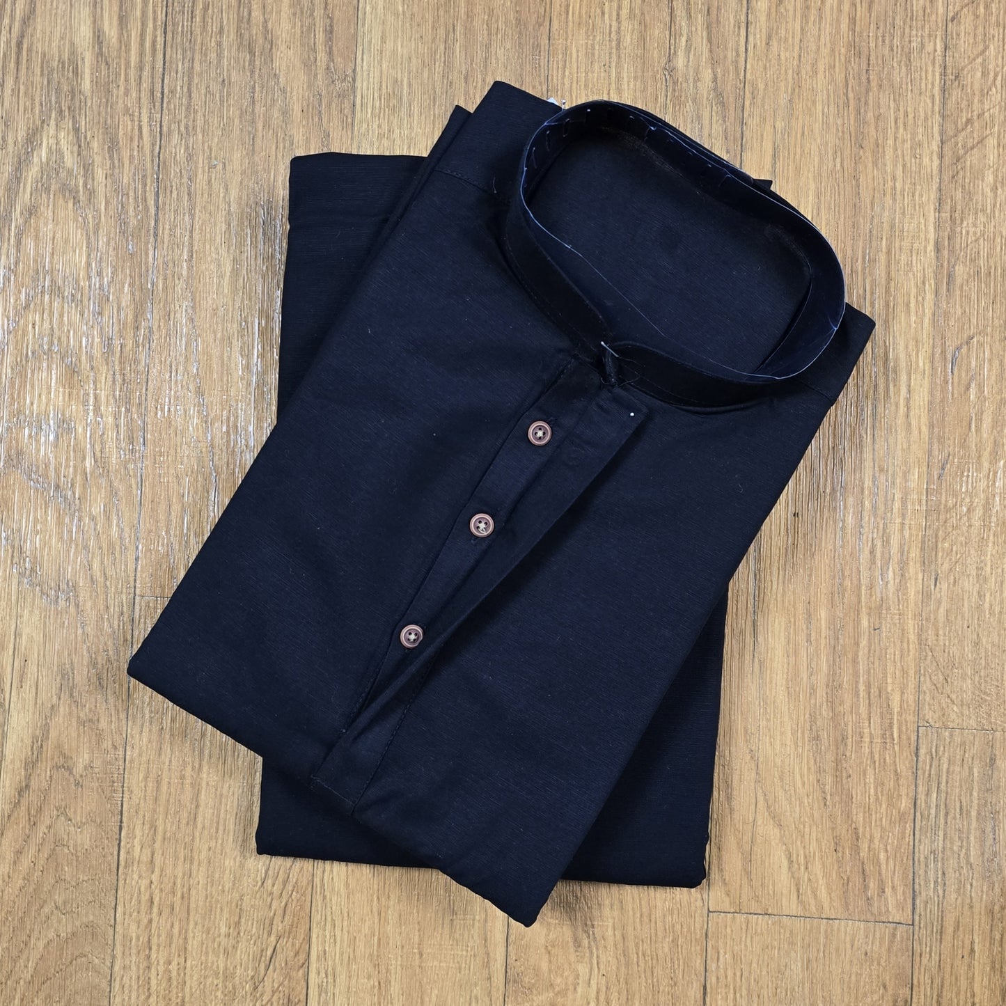 Folded black mandarin collar shirt with brown buttons on wooden floor