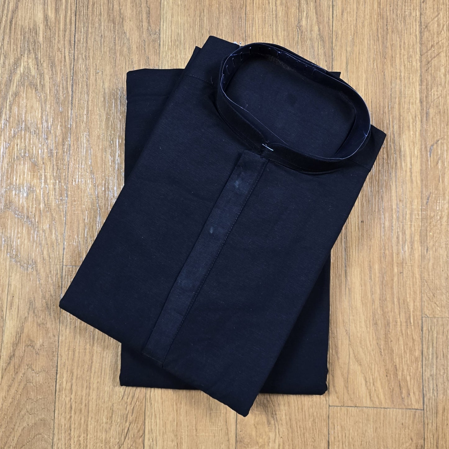 Folded black mandarin collar shirt with brown buttons on wooden floor