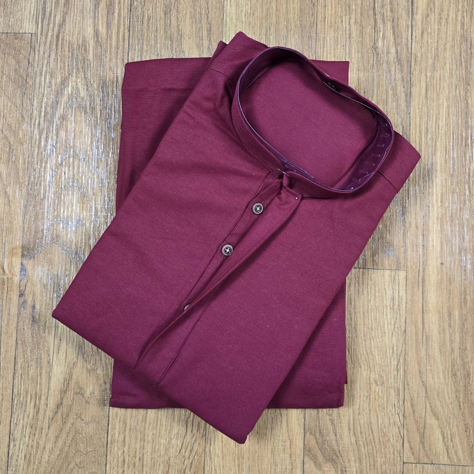 Folded maroon mandarin collar shirt on wooden floor