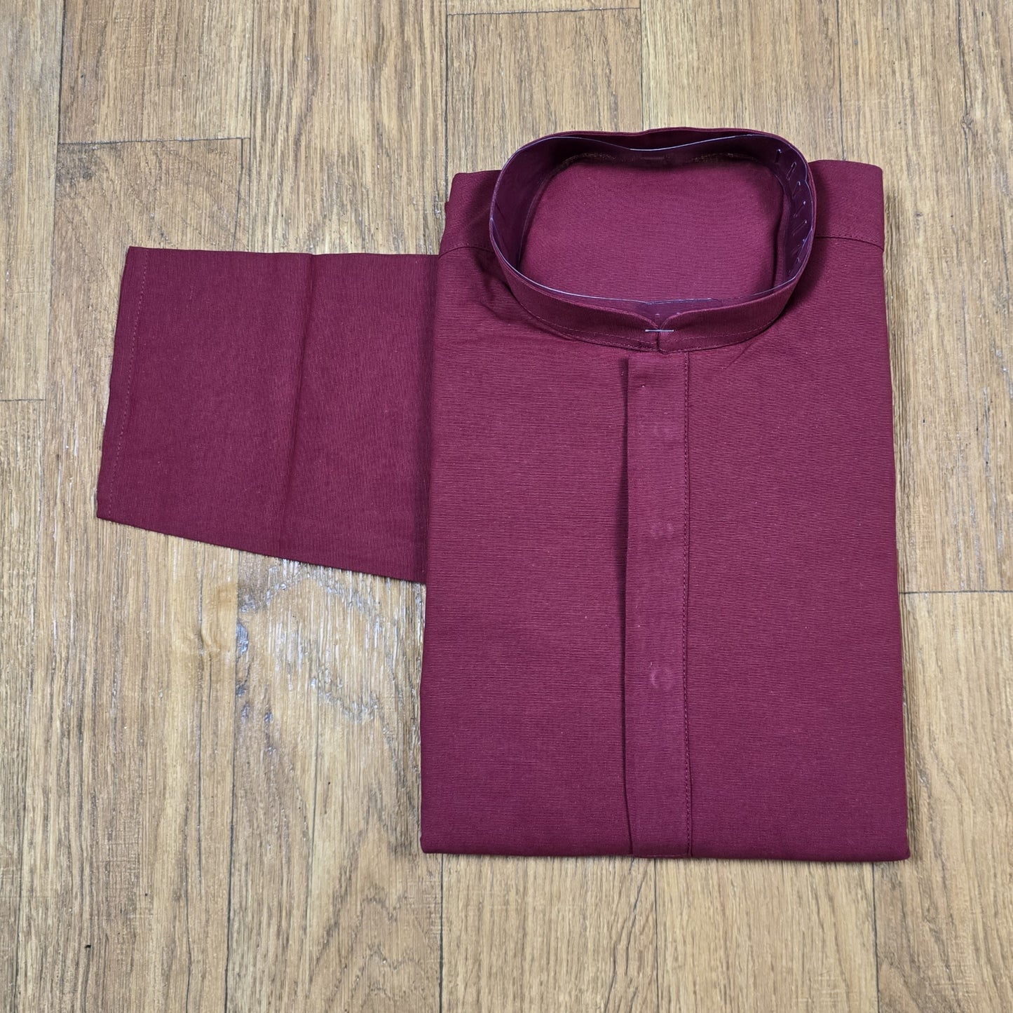 Folded maroon mandarin collar shirt on wooden floor
