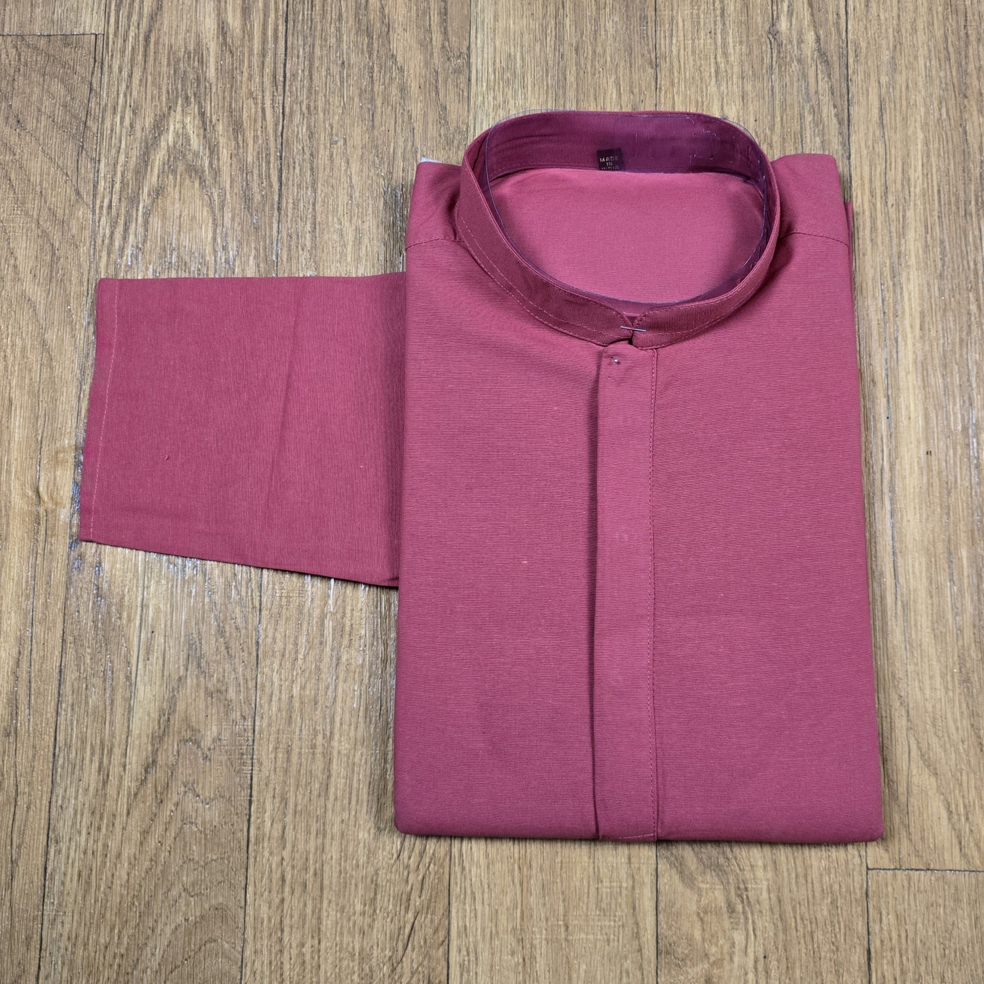 Folded dusty rose mandarin collar shirt on wooden floor