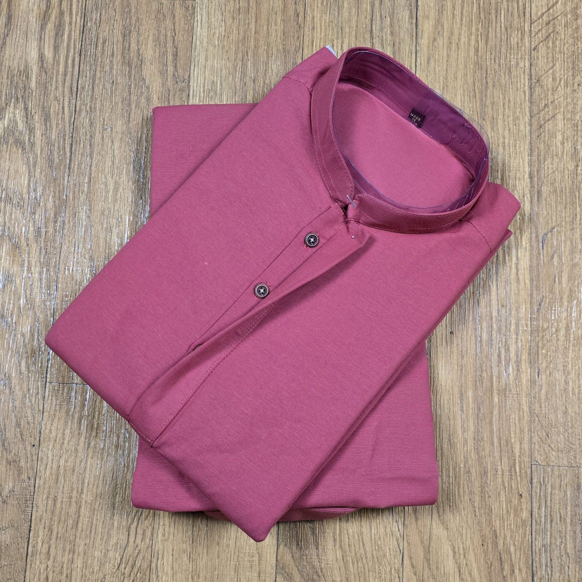 Folded dusty rose mandarin collar shirt on wooden floor