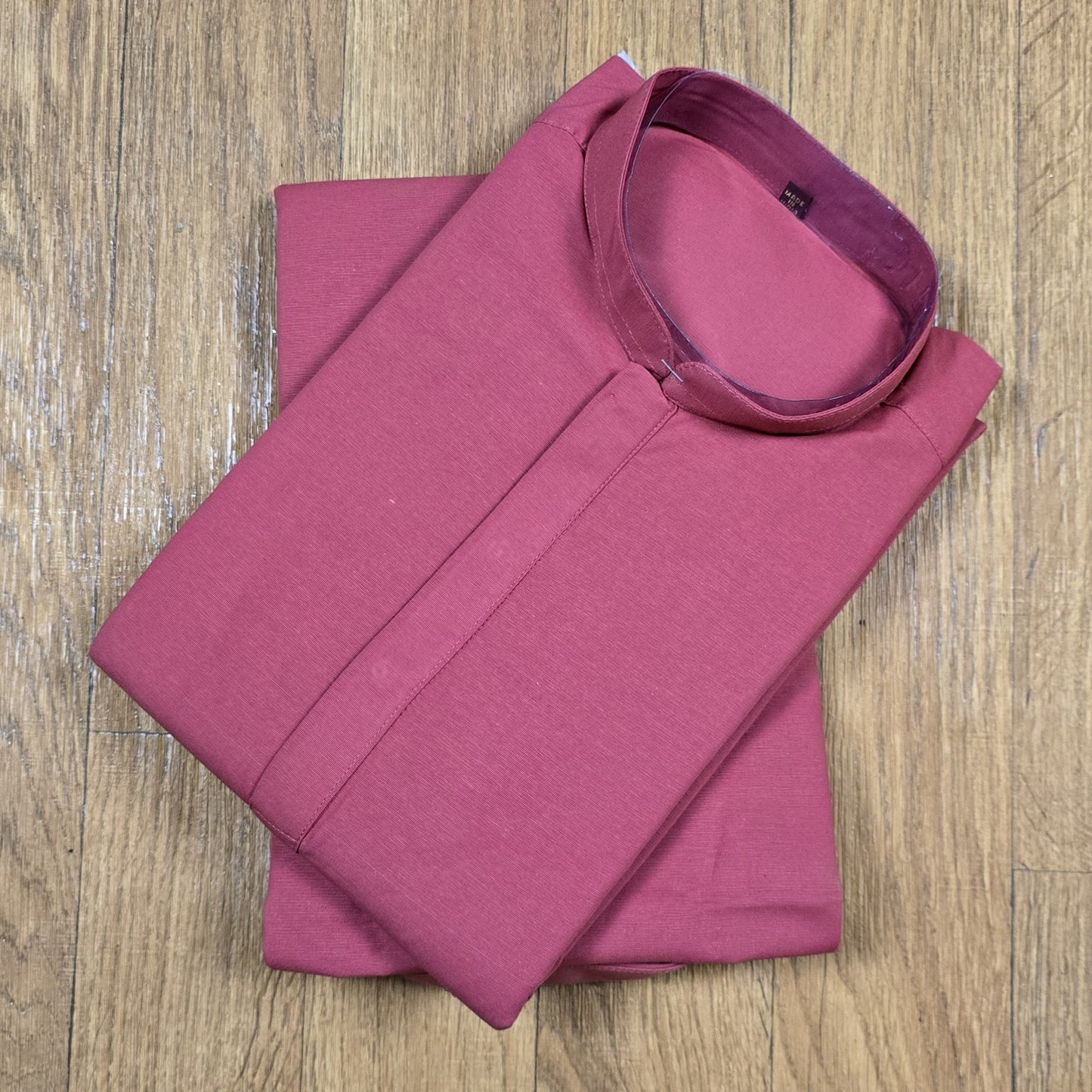 Folded dusty rose mandarin collar shirt on wooden floor