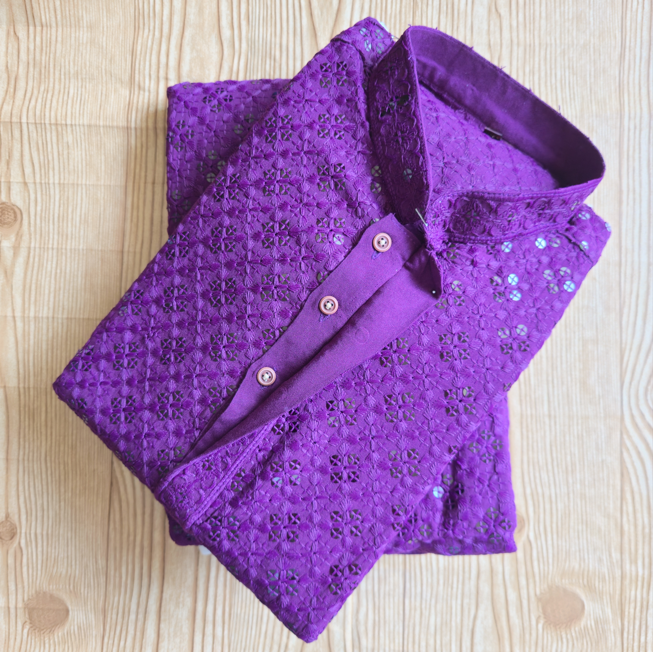 Folded purple sequin shirt on a wooden surface